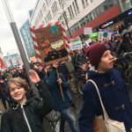 Foto eines Demonstrationszugs, zwei Gruppenmitglieder der Sippe Manul im Vordergrund. Im Hintergrund sind Fridays for Future Plakate zu sehen.