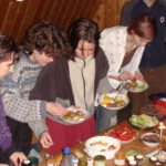 Fünf Pfadfinder und Pfadfinderinnen stehen vor einem Buffet, und legen Essen auf ihre Teller.