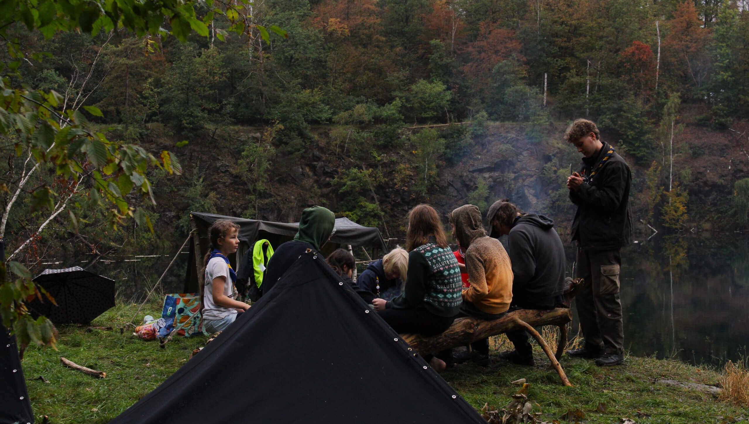 Ein paar Pfadfinder und Pfadfinderinnen sitzen zusammen am Lagerfeuer, im Hinetrgrund sieht man einen Steinbruch.