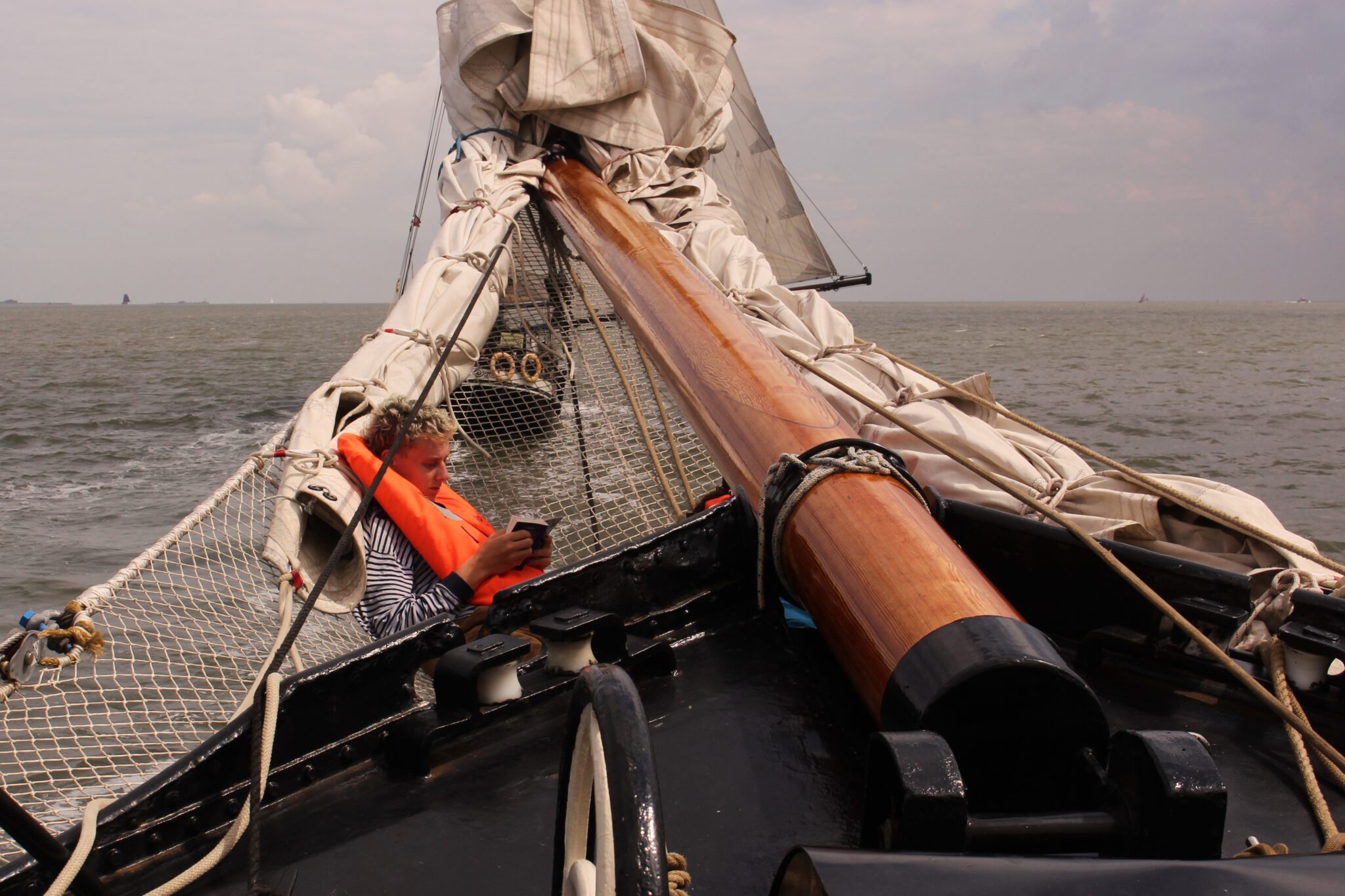 Im Klüvernetz eines Segelschiffs liegt ein Pfadfinder und liest ein Buch