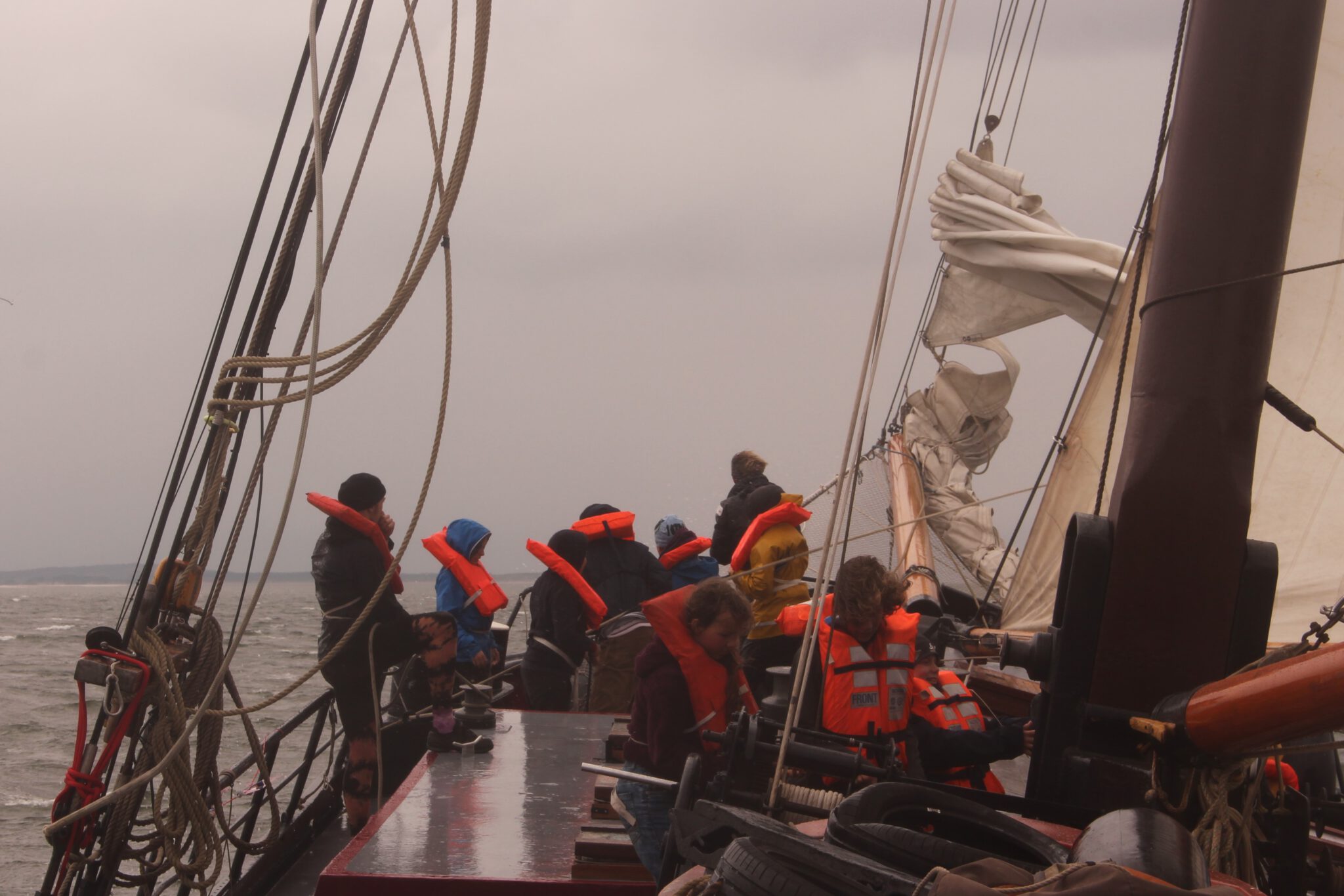 Bei stürmischem Wetter stehen ein paar Pfadfinder*innen in Rettungswesten an Bug eines Segelschiffs.