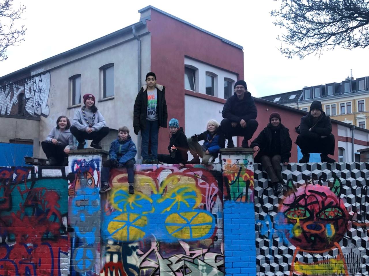 Die Gruppenmitglieder der Sippe Azules sitzen auf einer Graffitibemalten Mauer und posen für das Gruppenbild.