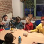 Um einen Tisch herum sitzen ein paar Kinder und drei Gruppenleiterinnen. Sie machen einen Abschlusskreis und halten sich an den Händen.